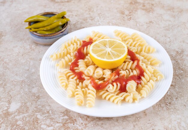 Porción pequeña de pimiento en escabeche con una ración de macarrones sobre superficie de mármol.