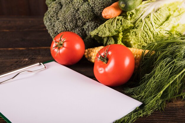 Portapapeles en blanco y verduras crudas frescas en el escritorio