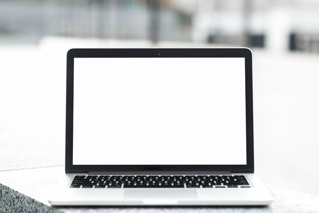 Un portátil abierto que muestra una pantalla en blanco en blanco en un banco contra un fondo borroso
