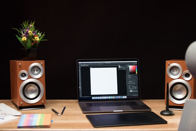 Portátil sobre la mesa con altavoces y flores.