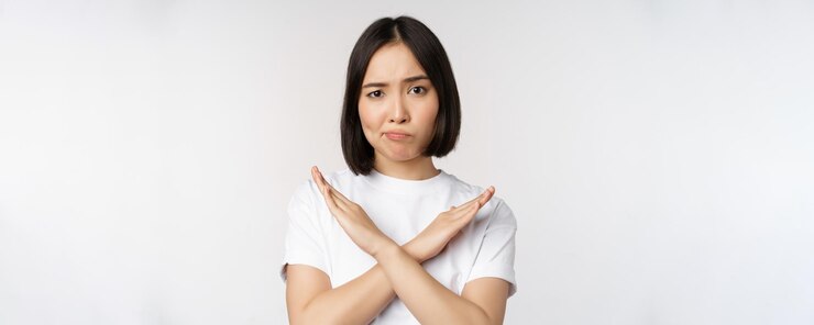 Photo Gratis portrait of asian korean woman showing stop prohibition gesture showing arm cross sign standing in tshirt over white background copy space