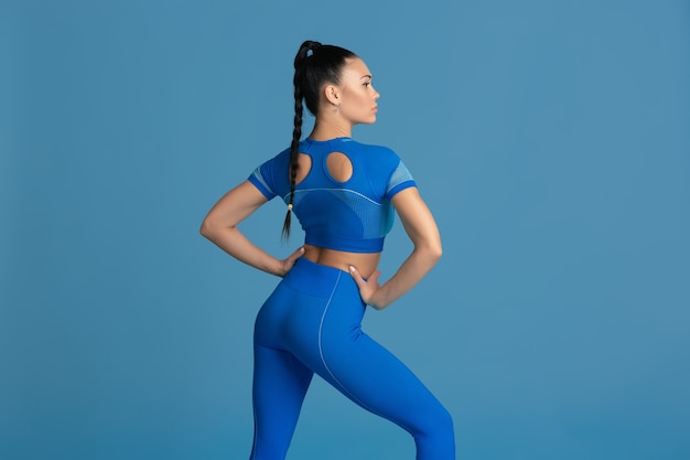 Posando sensual. Hermosa joven atleta practicando, monocromo retrato azul. Entrenamiento modelo morena de ajuste deportivo. Concepto de bienestar, estilo de vida saludable, belleza, movimiento y acción.