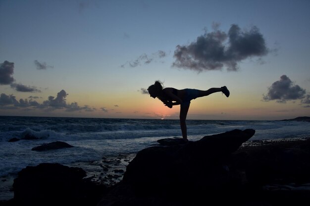 Pose de equilibrio de yoga Warrior 3 con sol saliendo sobre el océano