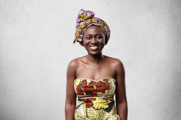 Foto gratuita positiva alegre mujer africana con un bonito vestido colorido sonriendo ampliamente, mostrando sus dientes blancos, sintiéndose feliz y relajada, disfrutando de un buen día. personas y estilo de vida