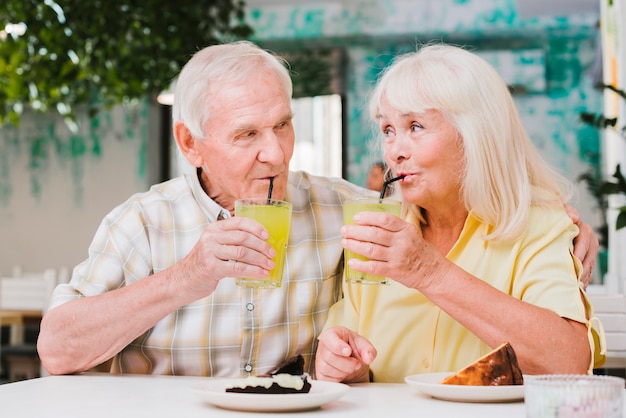 Positiva pareja de ancianos abrazándose en la cafetería disfrutando de una bebida refrescante y postre