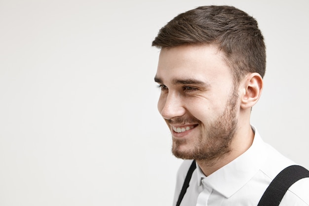 Foto gratuita positividad, alegría, felicidad y emociones humanas genuinas. retrato de apuesto joven empresario barbudo con camisa blanca con tirantes, regocijándose por los resultados y beneficios de su proyecto empresarial