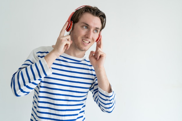 Positivo joven guapo en auriculares escuchando música y mirando de lejos.