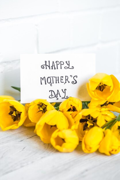 Postal del día de la madre y tulipanes amarillos sobre un fondo de madera clara, concepto de vacaciones