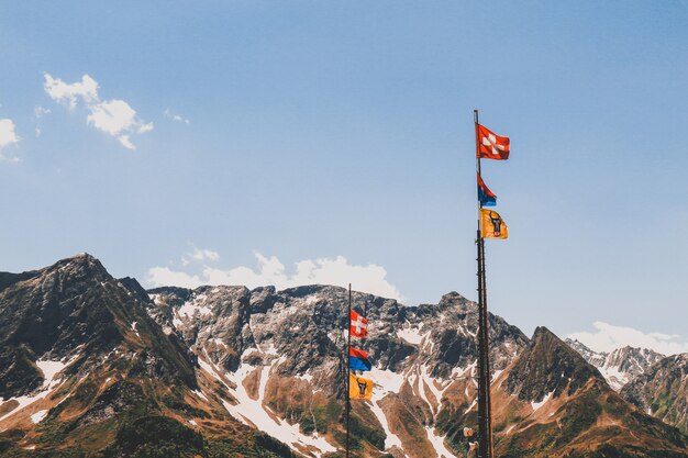 Postes con banderas en las hermosas montañas rocosas cubiertas de nieve bajo el cielo nublado