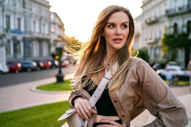 Postrait informal de la ciudad al aire libre de una elegante mujer rubia caminando sola divirtiéndose al atardecer