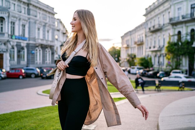 Postrait informal de la ciudad al aire libre de una elegante mujer rubia caminando sola divirtiéndose al atardecer