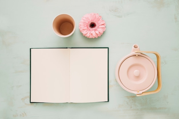 Pot y taza cerca de la flor y el cuaderno