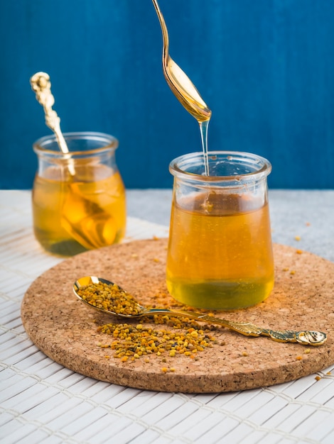 Pote de miel con polen de abeja en una cuchara sobre la montaña rusa de corcho