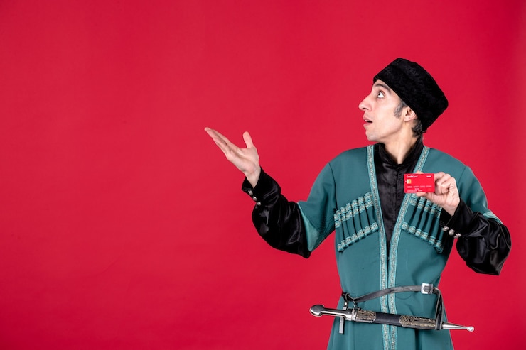 Photo Gratis potret pria azeri muda dengan kostum tradisional memegang kartu kredit di atas warna merah