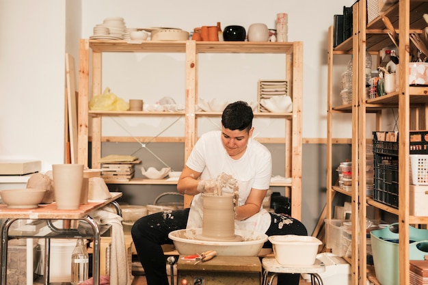 Potter femenino joven que forma un borde en el jarro en el taller