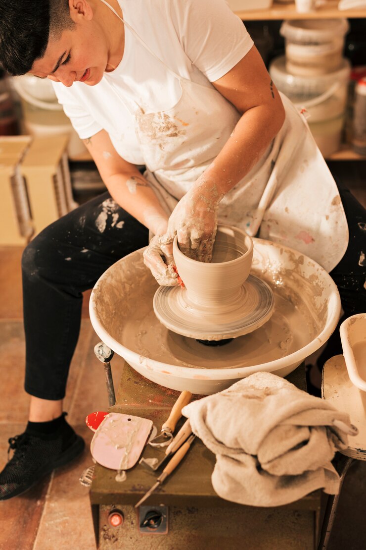 Foto gratuito potter de mujer alisando la superficie exterior de la olla en la rueda de alfarería