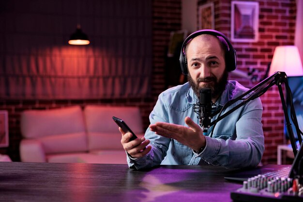 POV del creador de contenido revisando el producto del teléfono inteligente en la cámara, filmando video de podcast en estudio con luces de neón. Vloguero en línea haciendo recomendaciones de teléfonos móviles en transmisión en vivo por Internet.