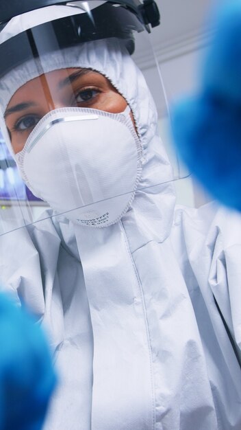 Pov de dentista en demanda de ppe contra covid trabajando en higiene bucal del paciente en consultorio dental con nueva normalidad. Estomatólogo con equipo de seguridad contra coronavirus durante el control de atención térmica del paciente.