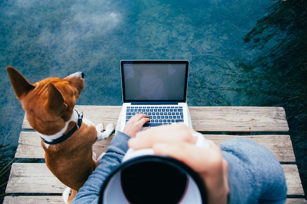 Foto gratuita pov de hombre beber café y trabajar en la computadora portátil en el lago