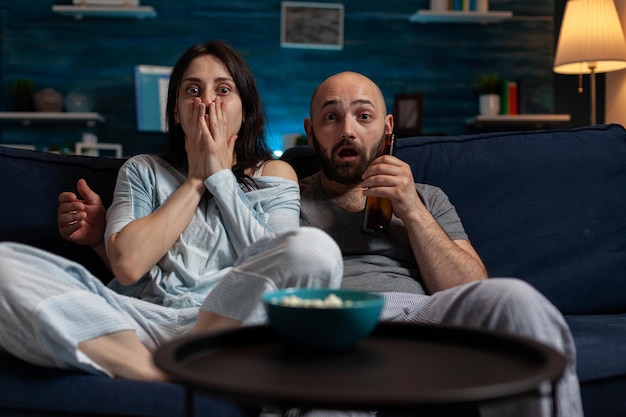 Pov de novia y novio sorprendidos viendo una película de terror en la televisión, sintiéndose aterrorizados. el hombre y la mujer tienen miedo y están ansiosos, miran una película aterradora en el canal de televisión para entretenerse.