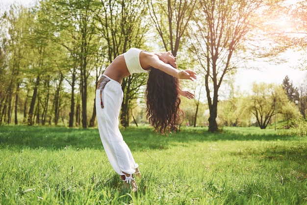Practicando yoga de una hermosa niña en la mañana con hierbas bajo las palabras del sol.
