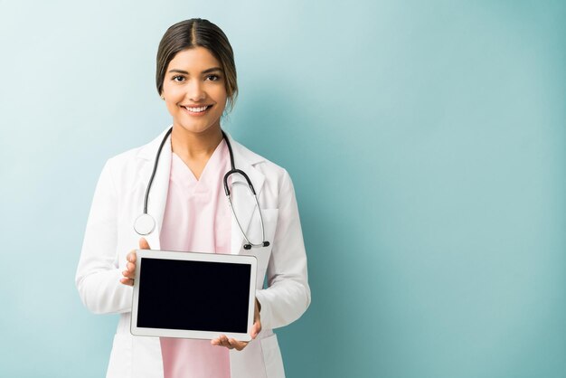 Una practicante feliz que muestra una tableta digital en blanco mientras se enfrenta a un fondo azul