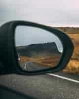 Foto gratuita pradera rodeada de rocas cerca de la carretera bajo un cielo nublado que se refleja en un espejo retrovisor