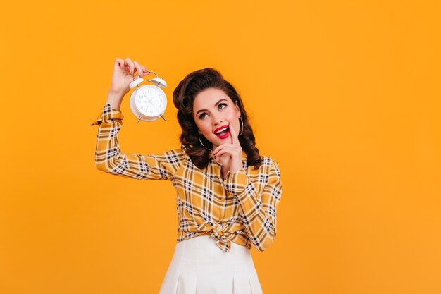 Preciosa chica modela con reloj grande. Foto de estudio de mujer europea bien vestida aislada sobre fondo amarillo.