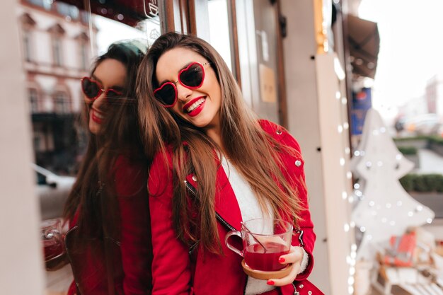 Preciosa modelo de mujer blanca lleva gafas de sol divertidas riendo cerca del restaurante