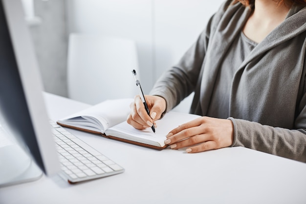 Prefiero el método de escritura de la vieja escuela. Retrato recortado de mujer ocupada haciendo notas en el cuaderno, mirando la pantalla de la computadora durante el tiempo de trabajo en la oficina, tratando de concentrarse y concentrarse en la tarea