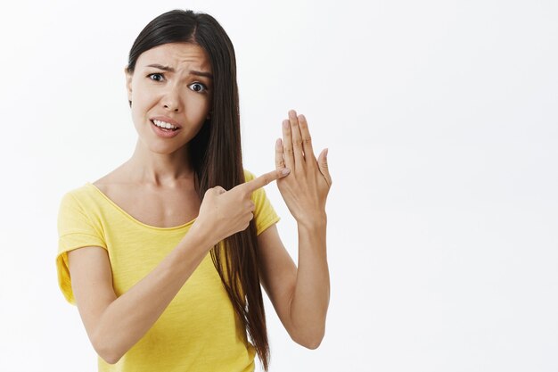 Pregunta joven novia enojada y confundida en camiseta amarilla mostrando la palma y apuntando con el dedo