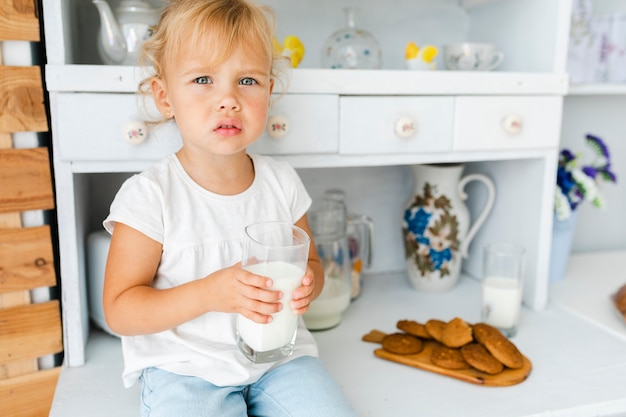 Foto gratuita preguntándose niña sosteniendo un vaso de leche