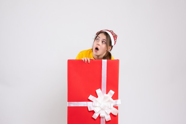 Se preguntó niña con gorro de Papá Noel de pie detrás de un gran regalo de Navidad en blanco