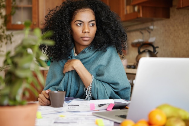 Preocupada hermosa mujer afroamericana tomando café en la mesa de la cocina