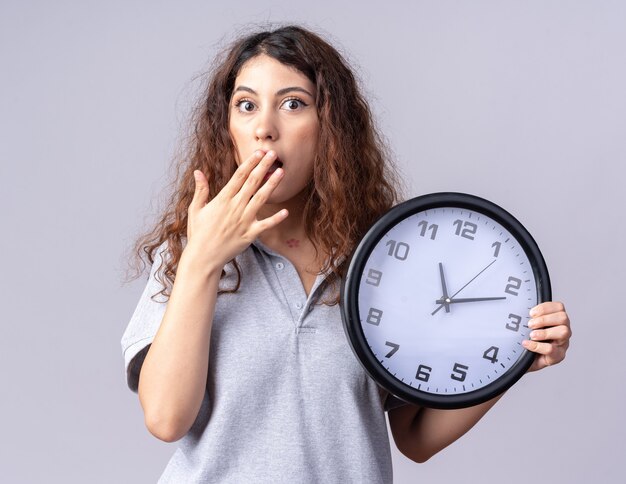 Preocupada joven bonita mujer caucásica sosteniendo el reloj manteniendo la mano en la boca