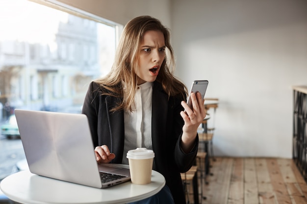 Preocupada joven empresaria en el café mirando el teléfono inteligente