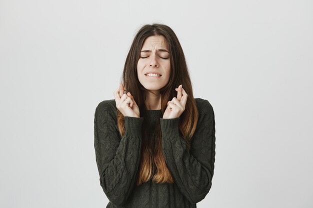 Preocupada joven linda pidiendo deseo con los ojos cerrados y los dedos cruzados