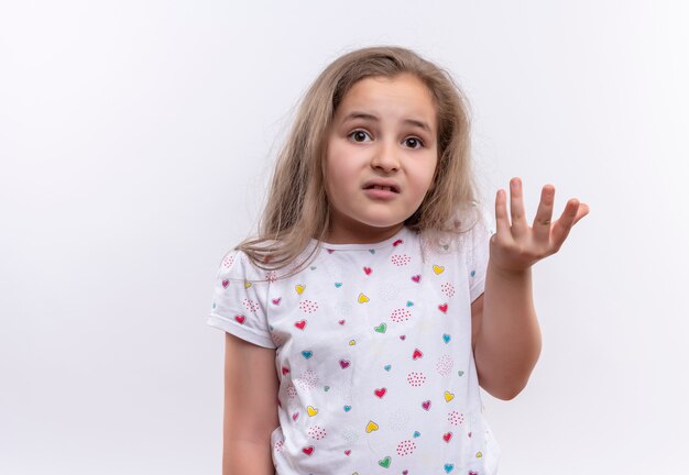 Preocupada niña de la escuela con camiseta blanca levantando las manos sobre la pared blanca aislada