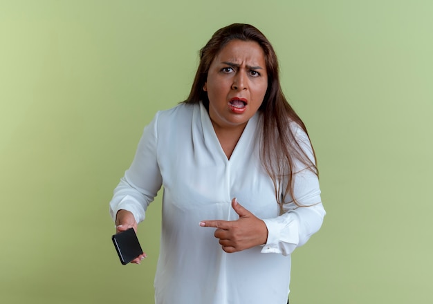 Foto gratuita preocupado casual mujer de mediana edad caucásica sosteniendo y apunta al teléfono