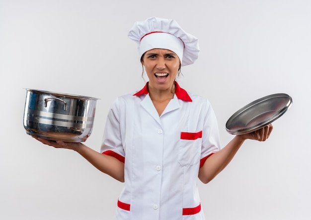 Preocupado joven cocinera vistiendo uniforme de chef sosteniendo una cacerola y tapa en la pared blanca aislada