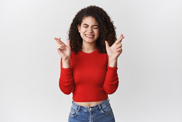 Preocupado nervioso esperanzado joven atractivo elegante mujer moderna pelo rizado cerrar los ojos apretar los dientes ansiosamente cruzar los dedos buena suerte rezando sueño hecho realidad esperando resultados importantes deseando