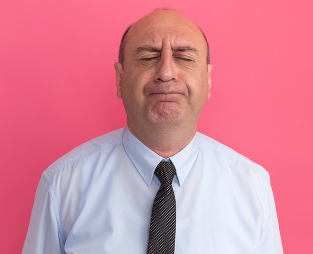 Preocupado con los ojos cerrados hombre de mediana edad vestido con camiseta blanca con corbata aislado en la pared rosa