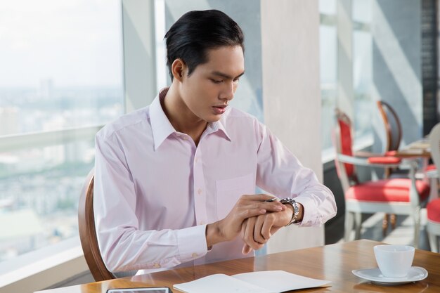 Preocupante joven asiático Hombre que mira el reloj en el Café