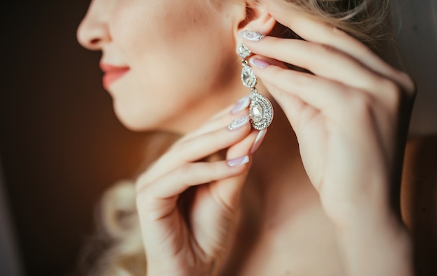 Preparación de la boda La novia hermosa, feliz viste los pendientes antes de casarse.