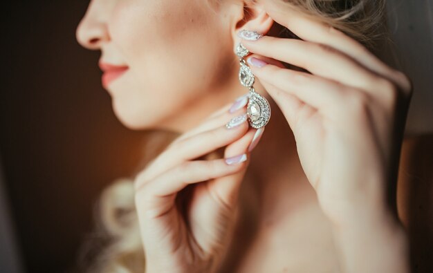 Preparación de la boda La novia hermosa, feliz viste los pendientes antes de casarse.