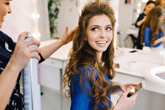 Preparación para celebrar en el salón de belleza de la modelo atractiva feliz sonriendo al estilista