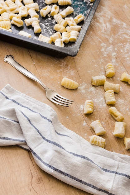 Preparación de ñoquis de pasta italiana fresca con tenedor y servilleta en mesa de madera