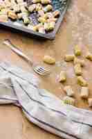 Foto gratuita preparación de ñoquis de pasta italiana fresca con tenedor y servilleta en mesa de madera