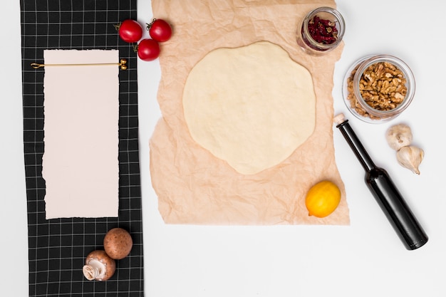 Preparación de pizza italiana casera rodeada de ingredientes y papel en blanco.