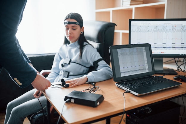 Foto gratuita preparación, poniendo electrodos en los dedos. chica pasa detector de mentiras en la oficina. haciendo preguntas. prueba de polígrafo